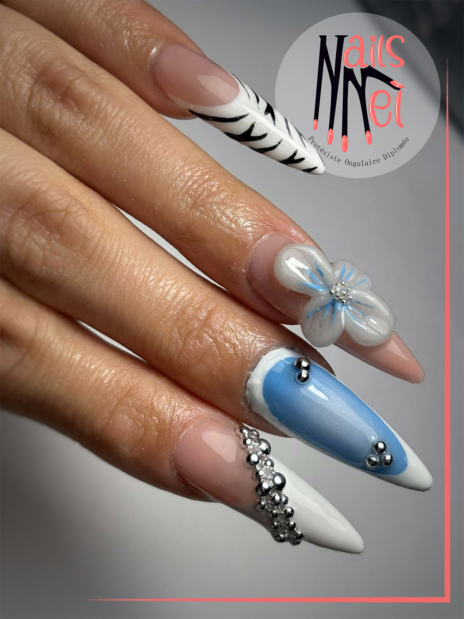 pose américaine réalisée à Hénin-Beaumont par Mélanie, prothésiste ongulaire, blanc et bleu avec accéssoires argentés et fleur en relief 3d